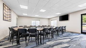 Une salle de conférence avec une longue table, de nombreuses chaises, un sol recouvert de moquette et une grande fenêtre.