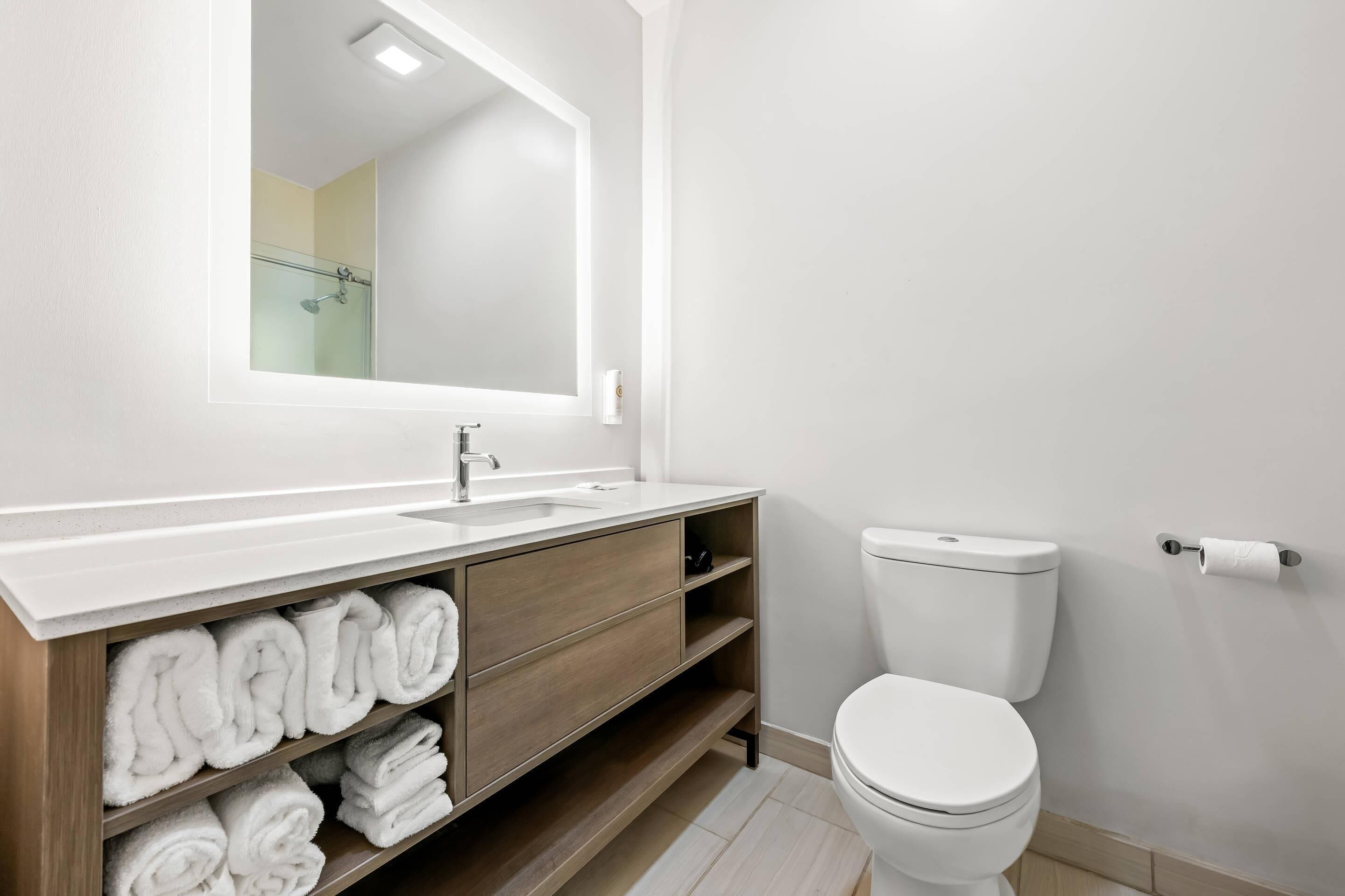 A modern bathroom with a white sink, wooden vanity, and a white toilet.
