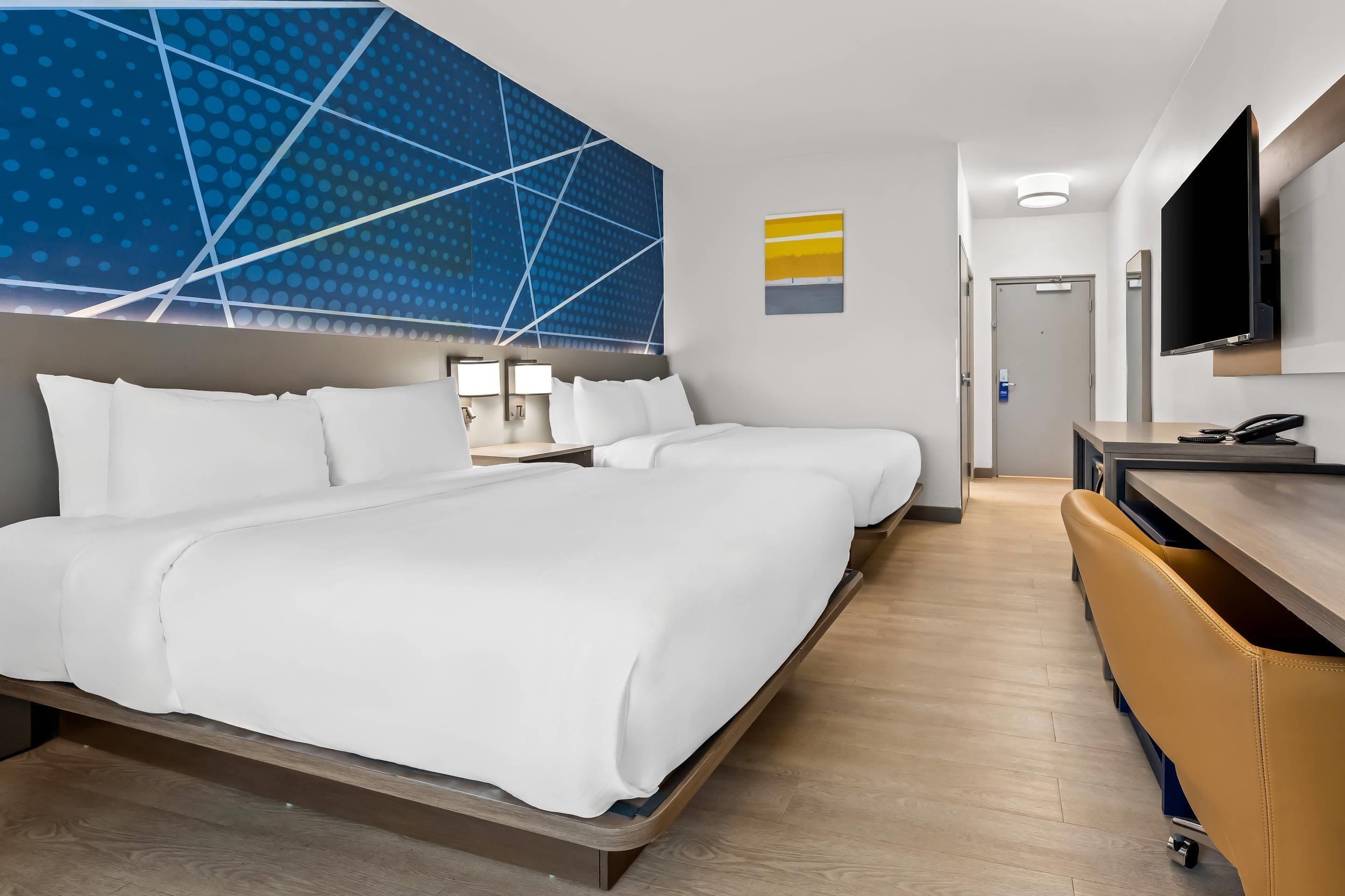 A hotel room with a large bed, a desk, a TV, and a modern wall design.