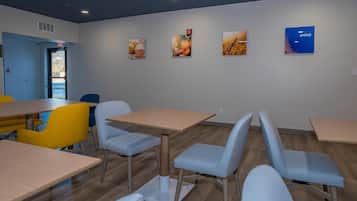 Un comedor moderno con mesas y sillas de madera, una puerta de salida azul y decoración en la pared.
