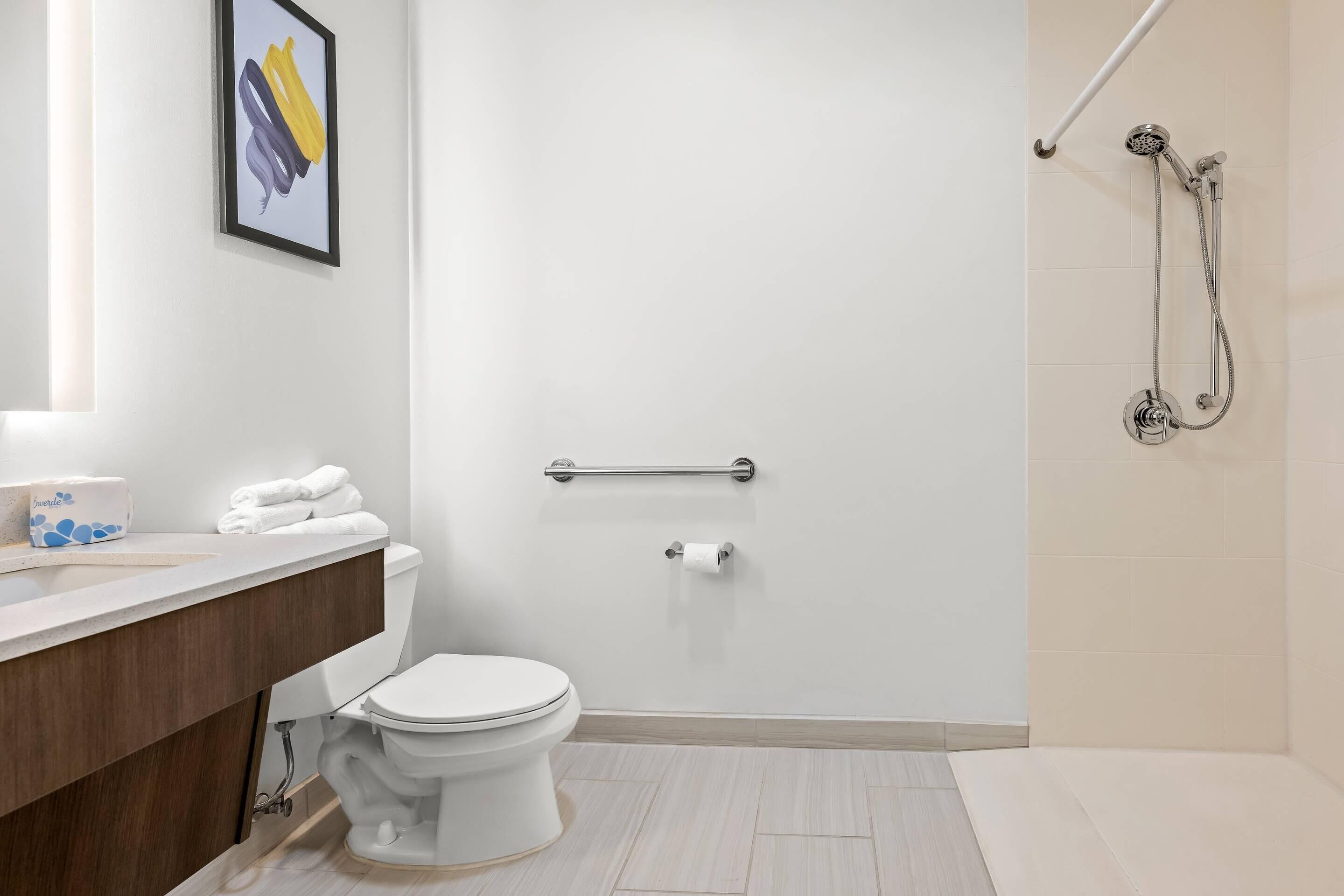 A modern bathroom with a toilet, a shower, and a vanity with a towel rack.