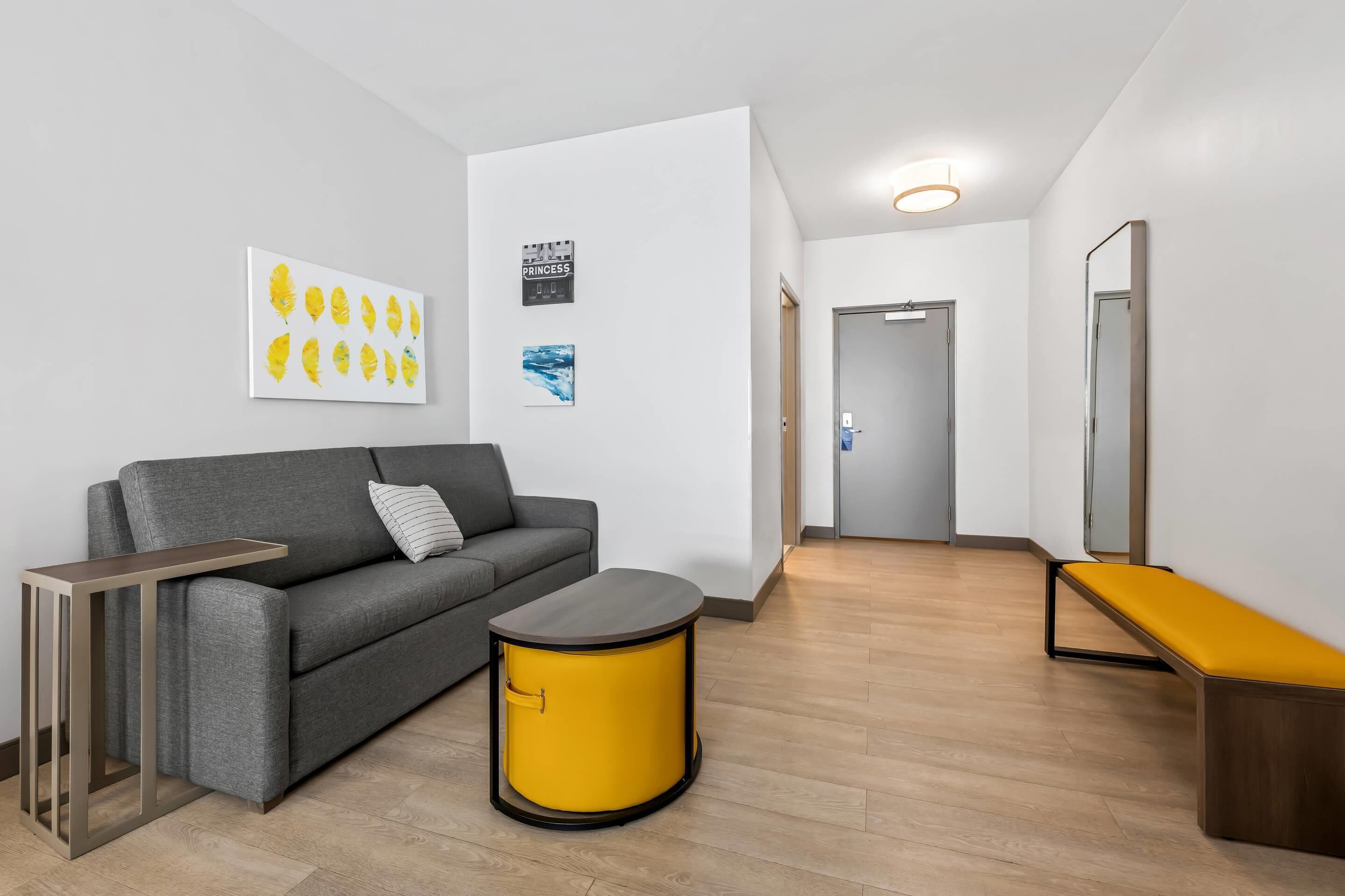 A modern living room with a grey sofa, a yellow side table, and a grey bench.