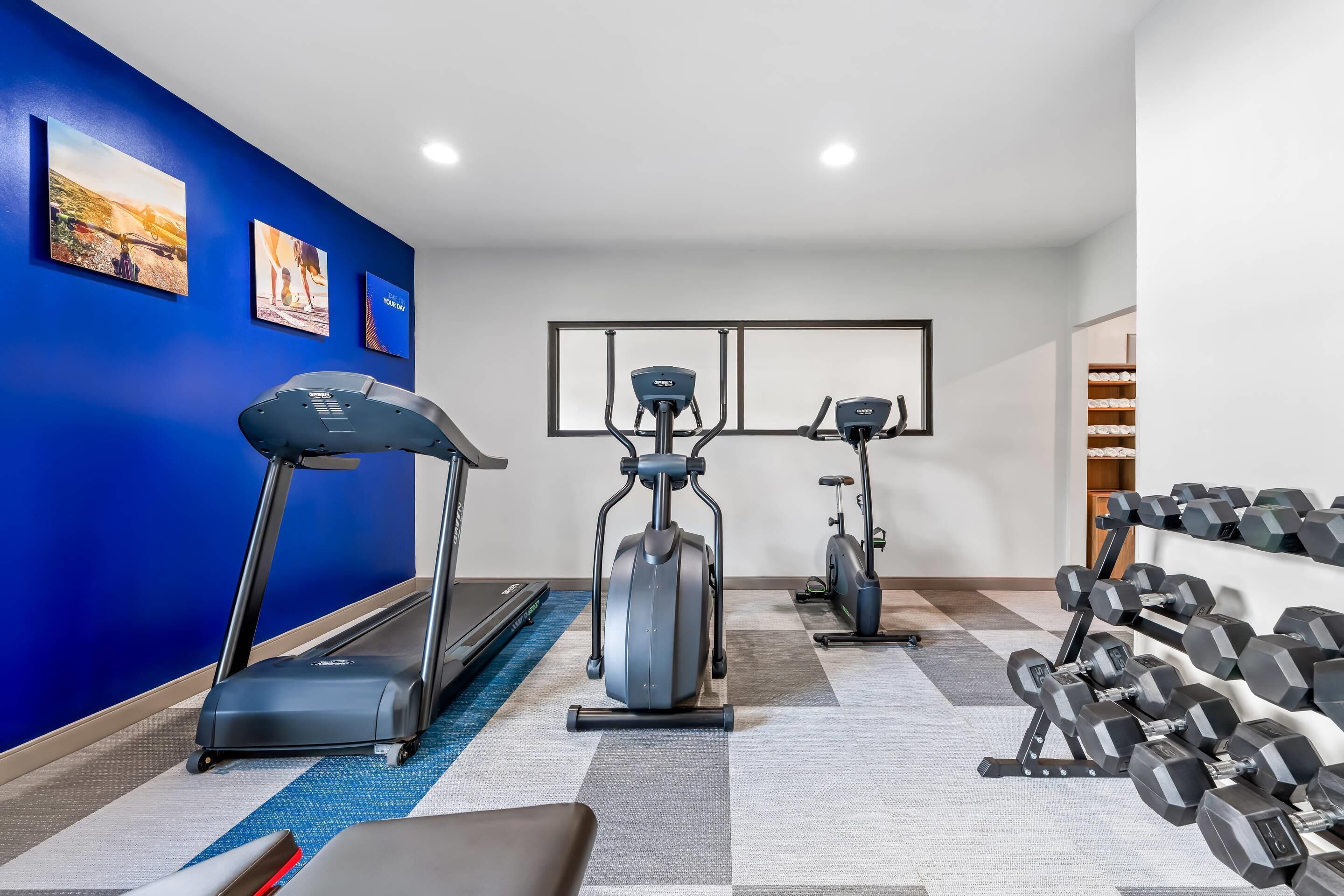 Une salle de sport à domicile équipée d’un tapis de course, d’un vélo elliptique et d’haltères.