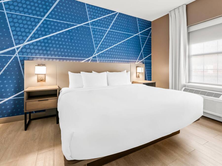 Habitació d'hotel amb un llit gran, una nit, una làmpada penjada a la paret i una finestra amb cortines.