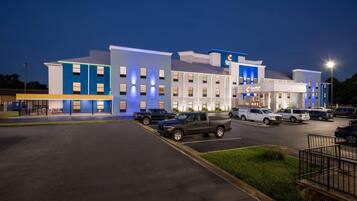 Een hotel met een modern design, met meerdere verdiepingen en een parkeerplaats met diverse voertuigen.