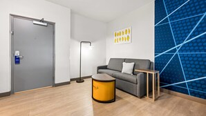 A modern, well-lit room with a grey sofa, a yellow side table, and a blue patterned wall. - Comfort Inn & Suites River City Decatur (Decatur)