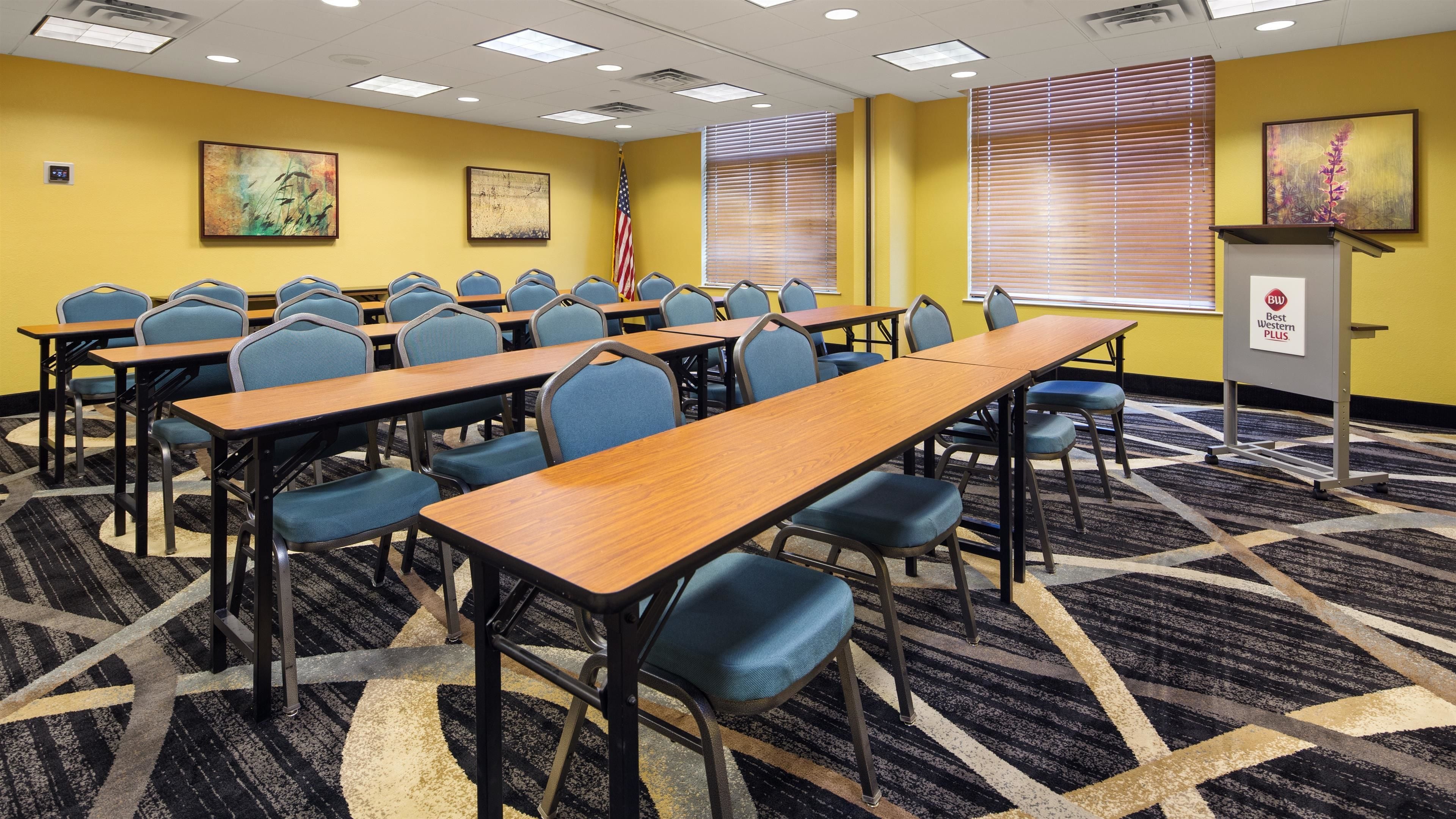 A conference room with multiple tables and chairs, a podium with a plaque, and an American flag.