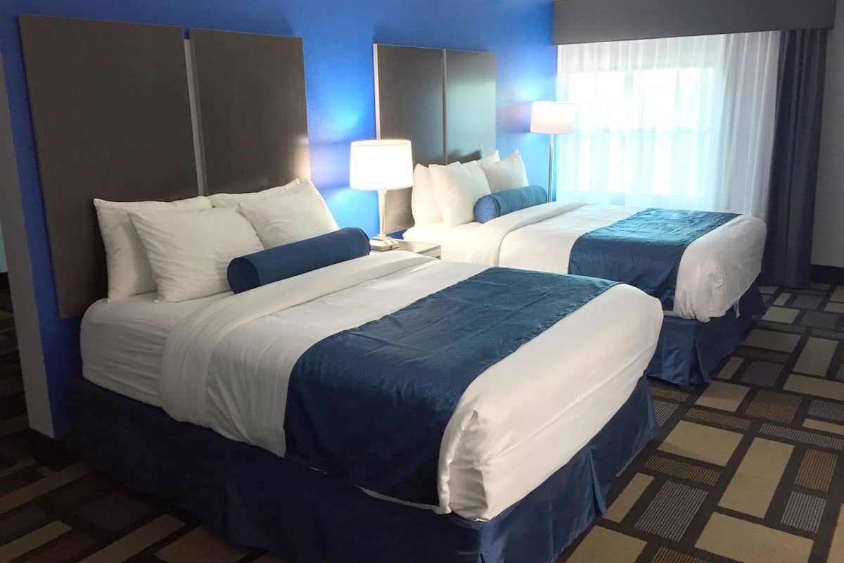 Una habitación de hotel con dos camas, un espejo grande, una mesita de noche y una ventana con cortinas.