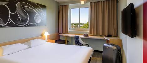 A hotel room with a bed, desk, chair, TV, and a suitcase.