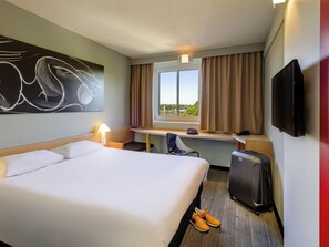 Habitación de hotel con cama, escritorio, silla, televisor y maleta.