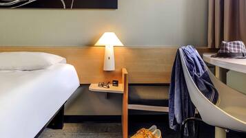 Una habitación de hotel con cama, mesita de noche con lámpara, un par de zapatos y una silla.
