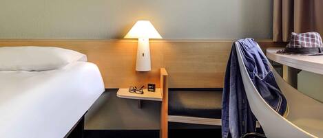 Una habitación de hotel con cama, mesita de noche con lámpara, un par de zapatos y una silla.