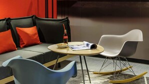 A modern room with a sofa, a small table, a rocking chair, and a wall with a large abstract design. - ibis Augsburg Koenigsplatz (Augsburg)
