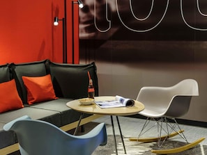 A modern room with a sofa, a small table, a rocking chair, and a wall with a large abstract design.