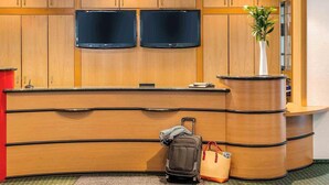 A reception desk with wooden paneling, two flat-screen TVs, a potted plant, a handbag, and a suitcase. - ibis Augsburg Koenigsplatz (Augsburg)