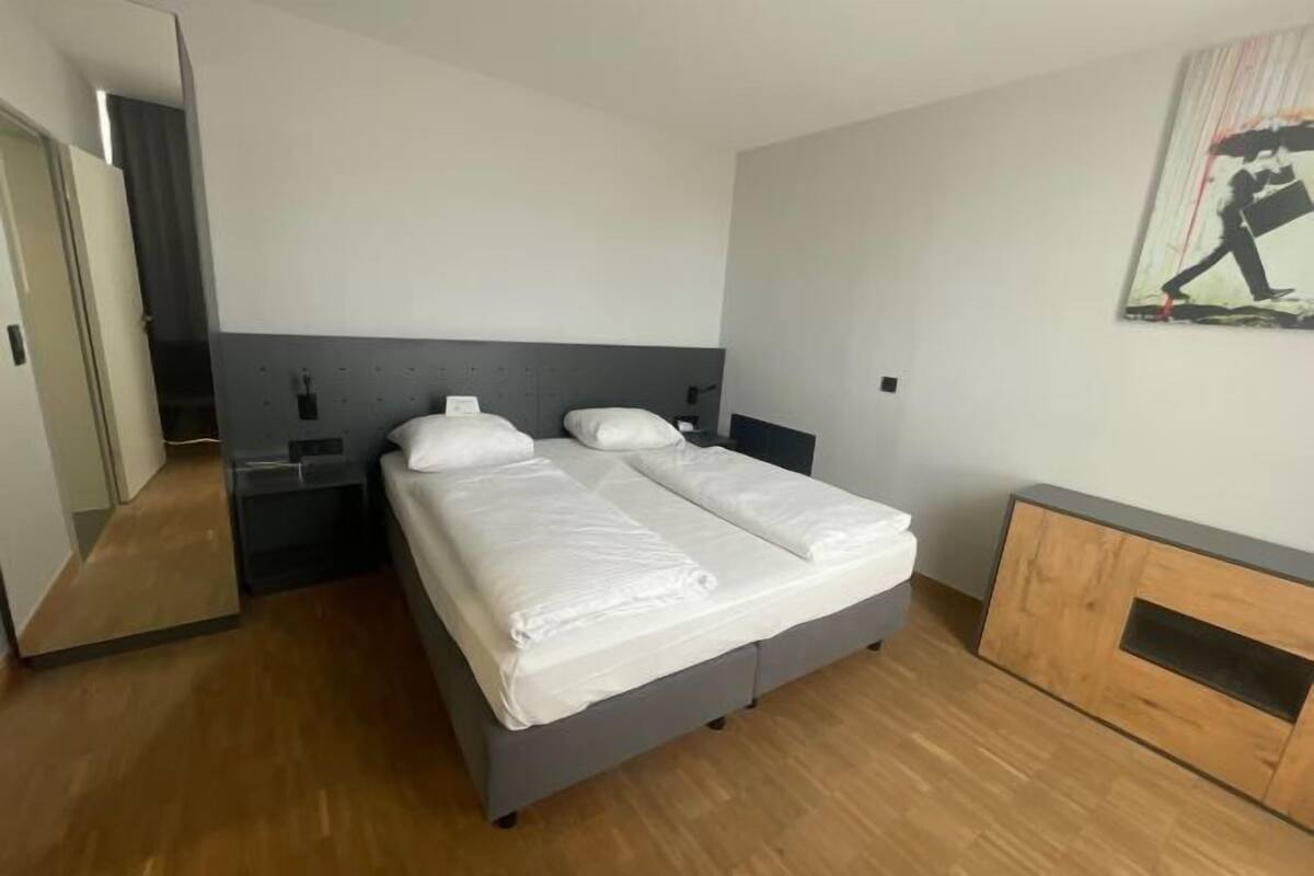 Quarto de hotel moderno com uma cama de casal, mesas de cabeceira, um espelho e um armário de madeira.