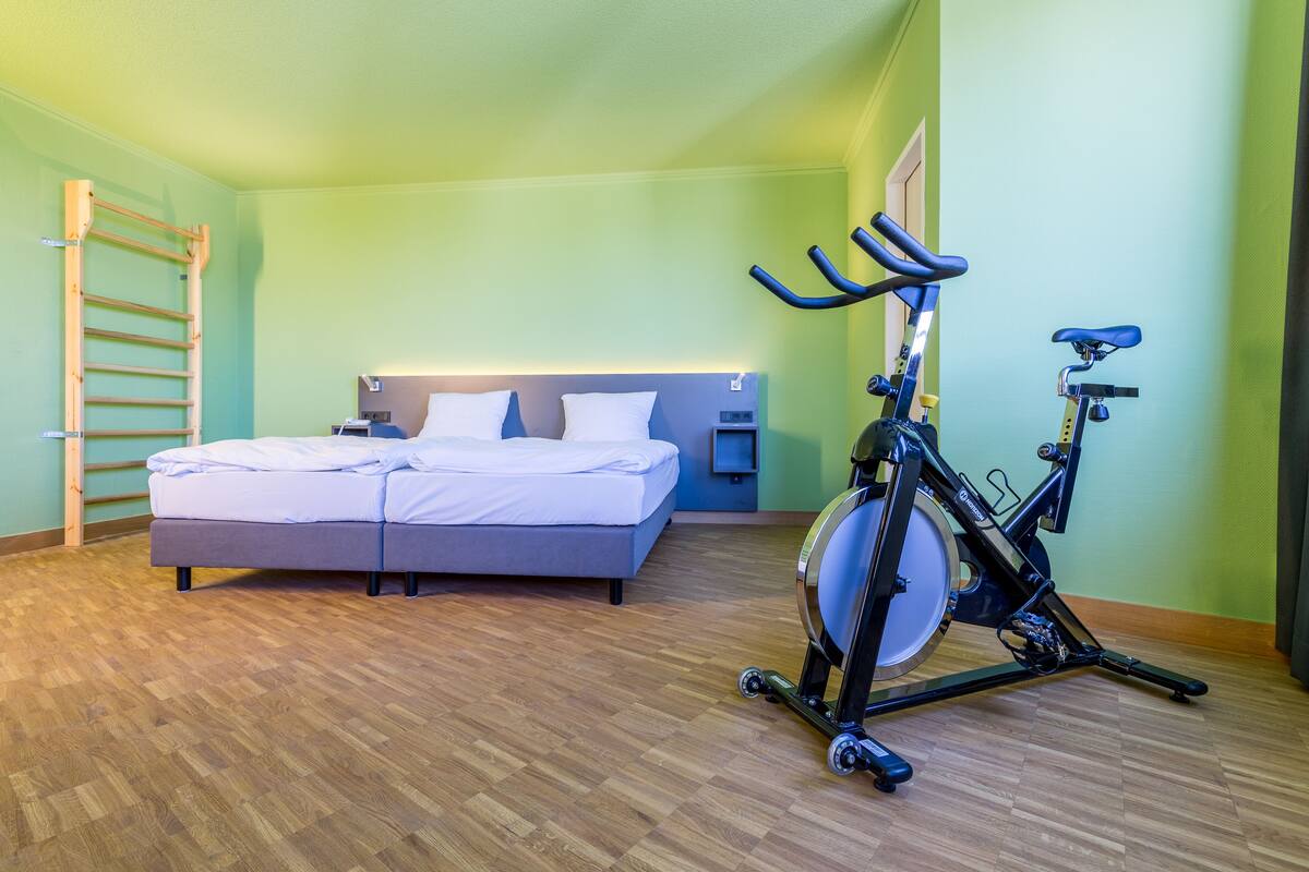 Quarto com cama, escada de madeira e uma bicicleta ergométrica.