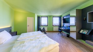 Ein Hotelzimmer mit Bett, Schreibtisch, Fahrrad und Blick auf die Stadt.