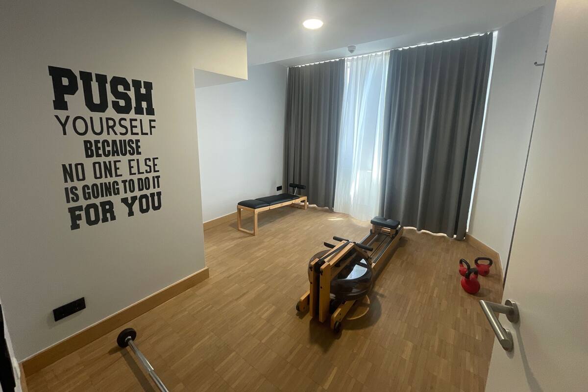 Uma academia com equipamentos de ginástica, um banco e uma frase motivacional na parede.