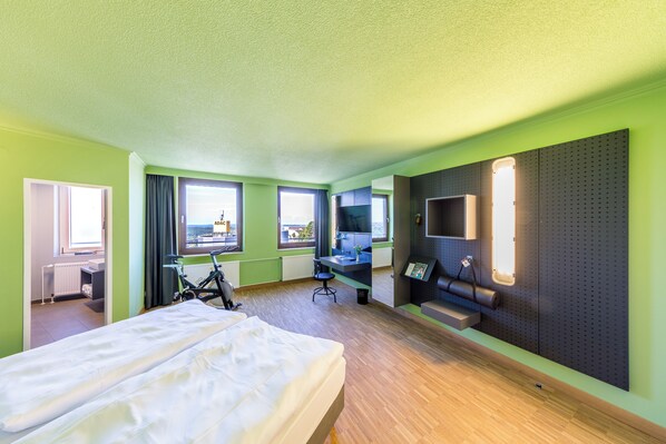 A hotel room with a bed, a desk, a chair, a sofa, a TV, and a window with a view.