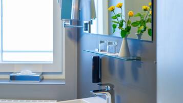 Un baño moderno con un lavamanos blanco, un espejo y un florero con flores amarillas.