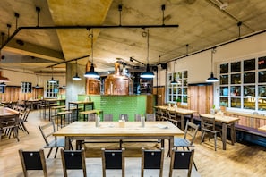 A spacious restaurant with wooden tables and chairs, hanging pendant lights, and a green-tiled bar area. - mk | hotel remscheid (Remscheid)