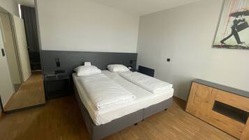 A modern hotel room with a large bed, bedside tables, a wardrobe, and a mirror.