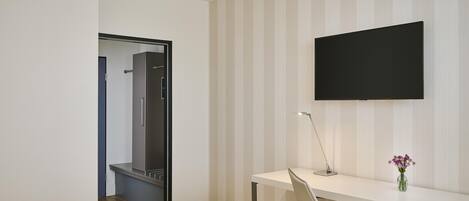 Habitación de hotel con cama, escritorio con silla, televisor de pantalla plana y espejo.