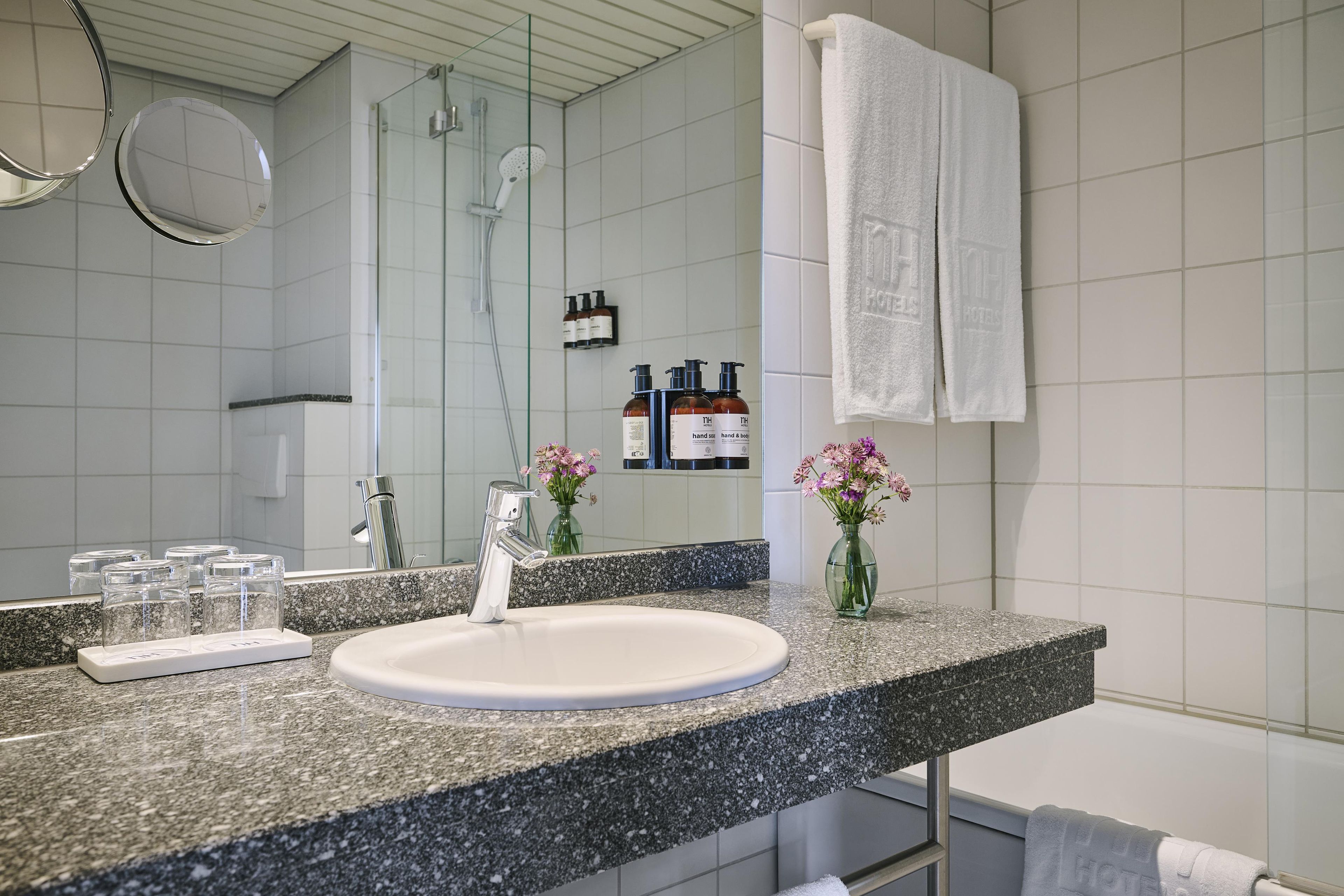 Een badkamer met een granieten aanrechtblad, een witte wasbak, een handdouche, een douchecabine met glazen wanden en een spiegel.