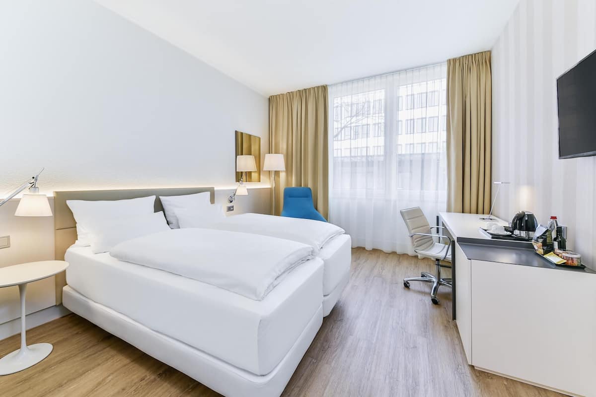 A hotel room with a bed, desk, chair, and a TV.