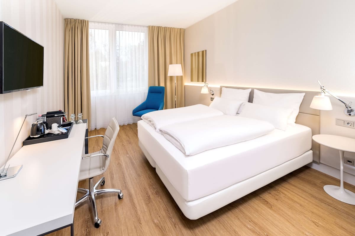 A hotel room with a large bed, a desk with a chair, a TV, and a window with curtains.