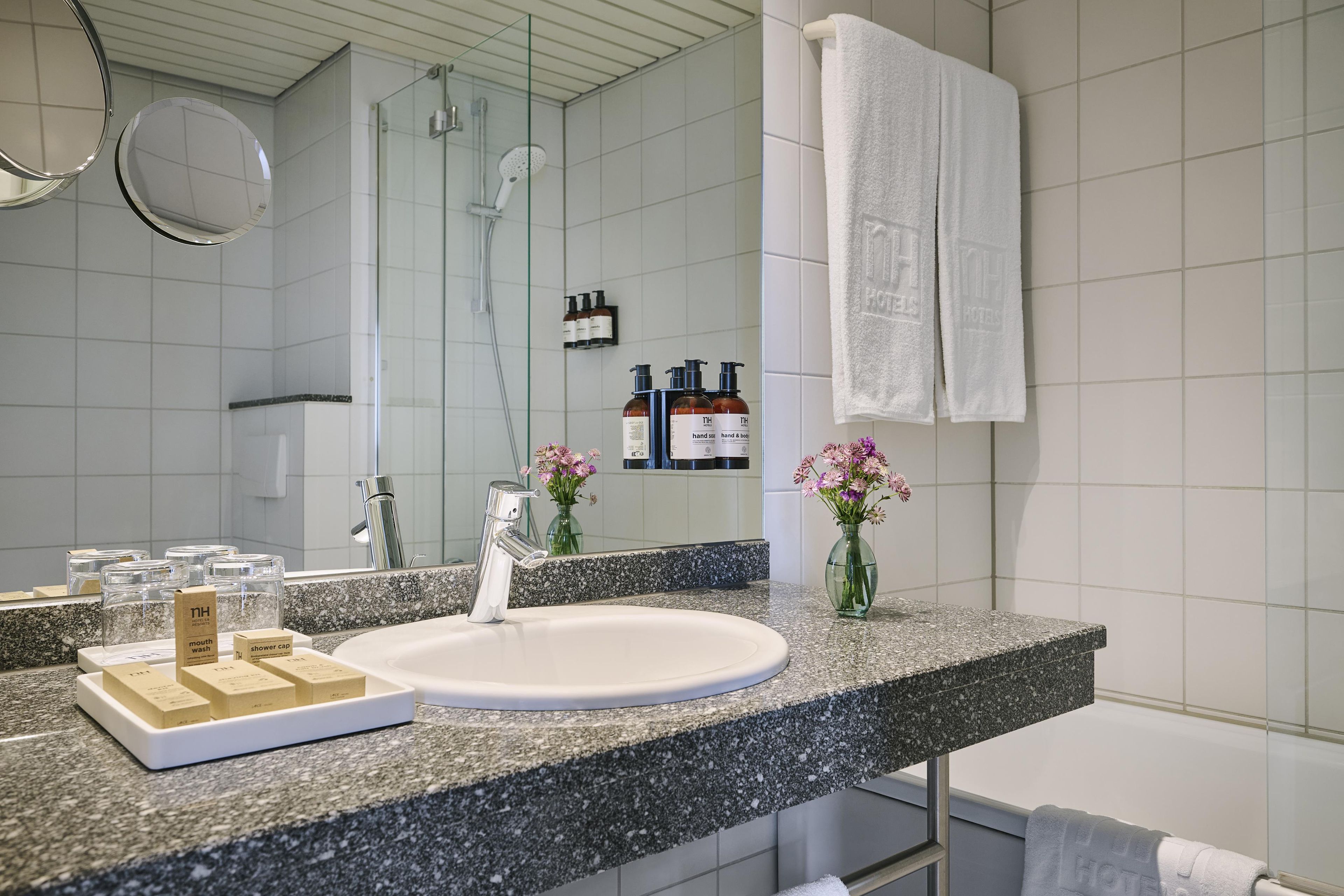 A modern bathroom with a granite countertop, a white sink, a handheld showerhead, and a glass shower enclosure.