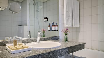 A modern bathroom with a granite countertop, a white sink, a handheld showerhead, and a glass shower enclosure.