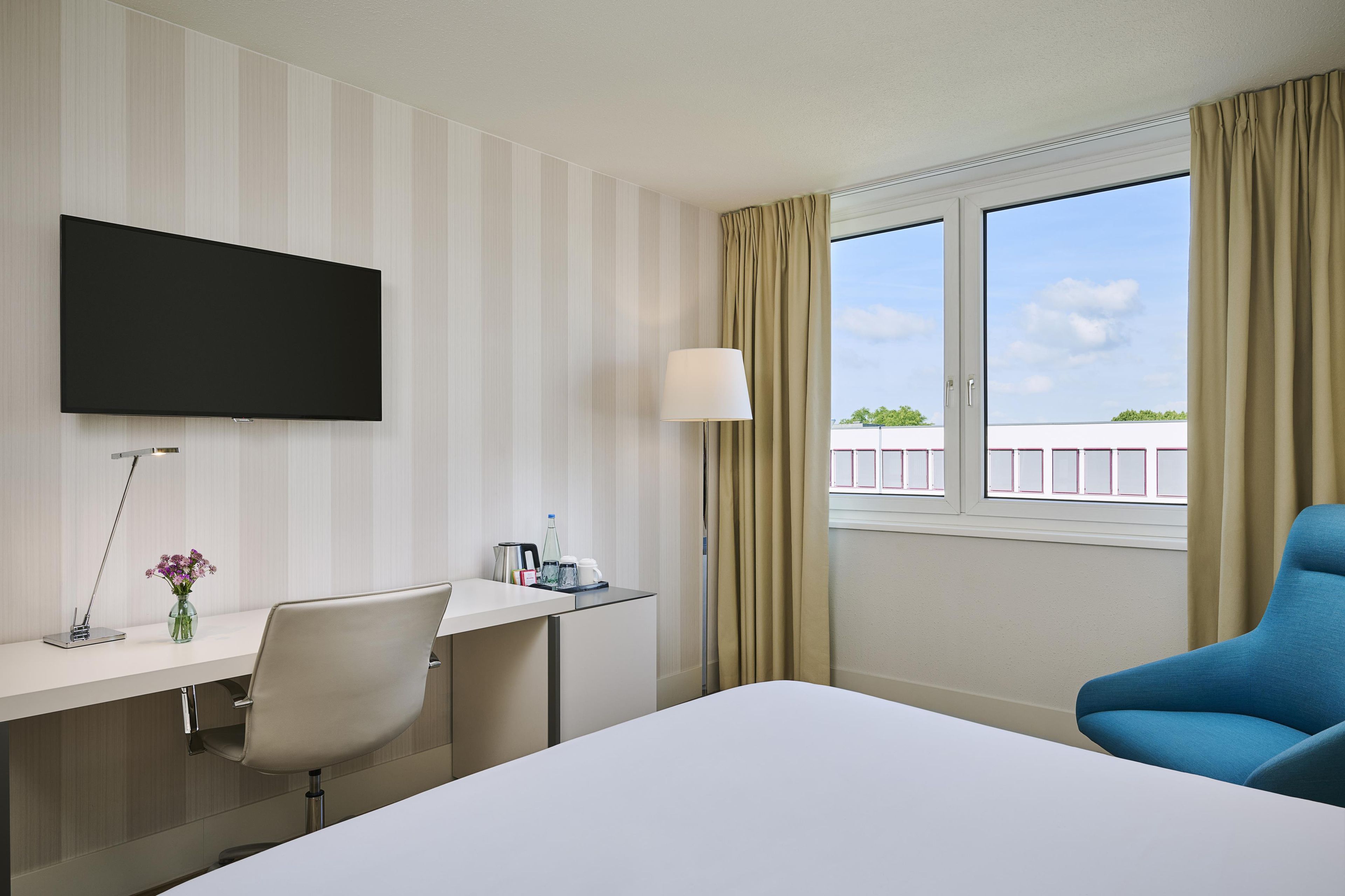 A hotel room with a bed, a desk, a chair, a television, and a window with curtains.