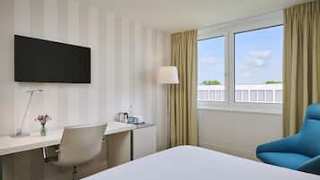 Habitación de hotel con cama, escritorio, silla, televisión y ventana con cortinas.