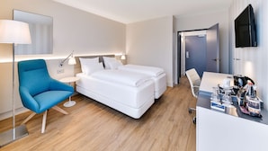A hotel room with a bed, a desk, a chair, a lamp, and a TV.