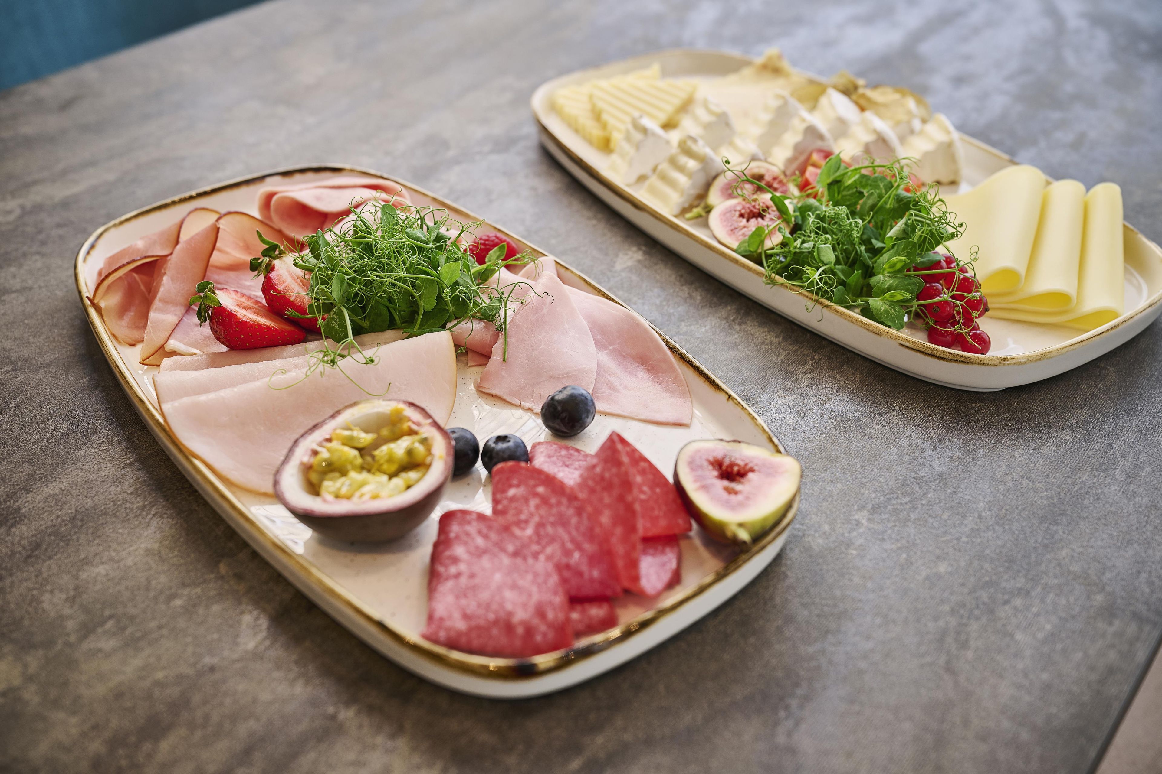 Two platters of food with various items including meats, fruits, and cheese.