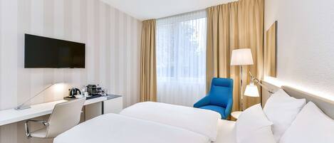 A hotel room with a bed, desk, chair, TV, and curtains.