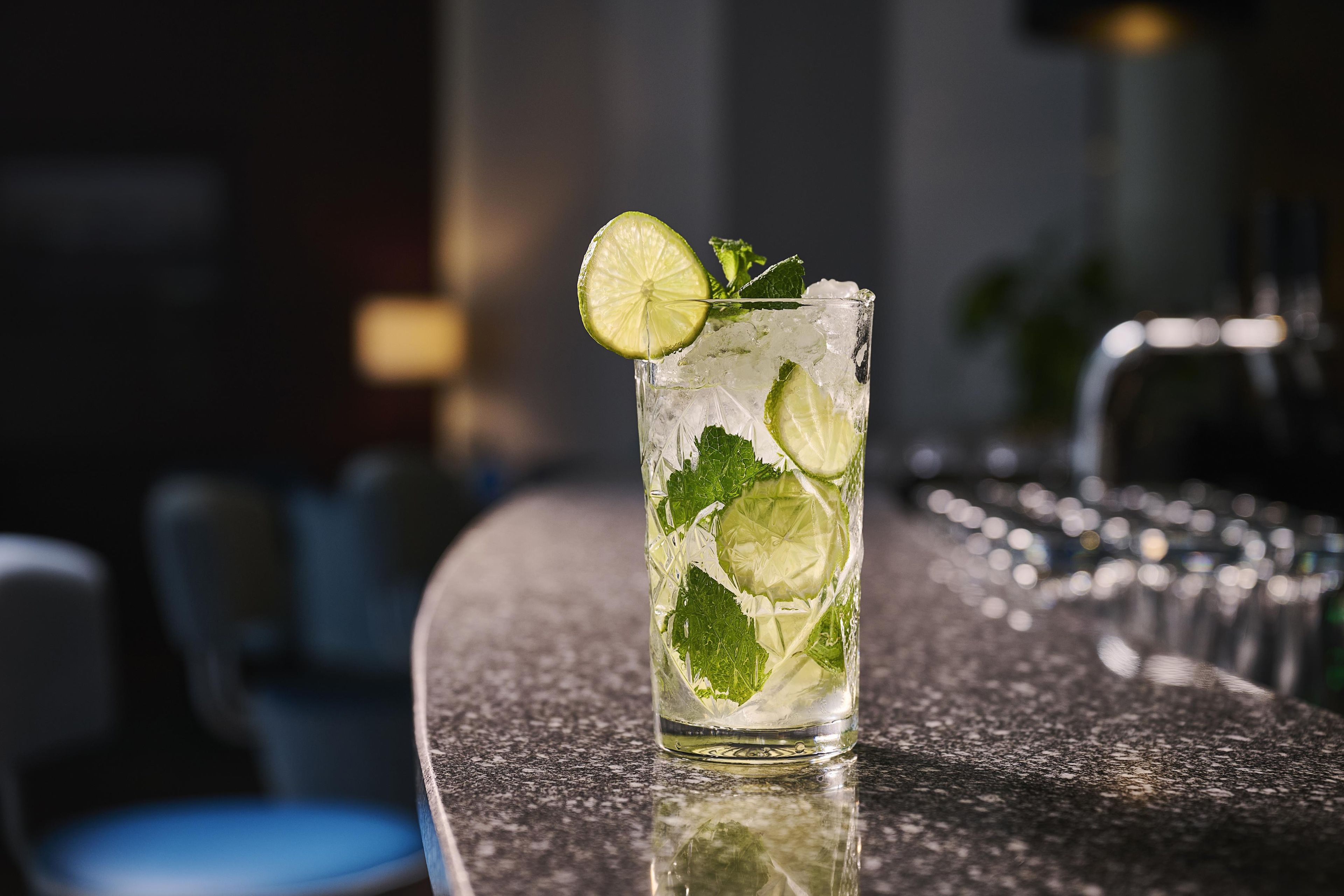 A tall glass with ice cubes and lime slices, placed on a bar counter.