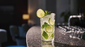 A tall glass with ice cubes and lime slices, placed on a bar counter.