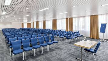 A conference room with rows of blue chairs, a wooden table, and a projector screen.