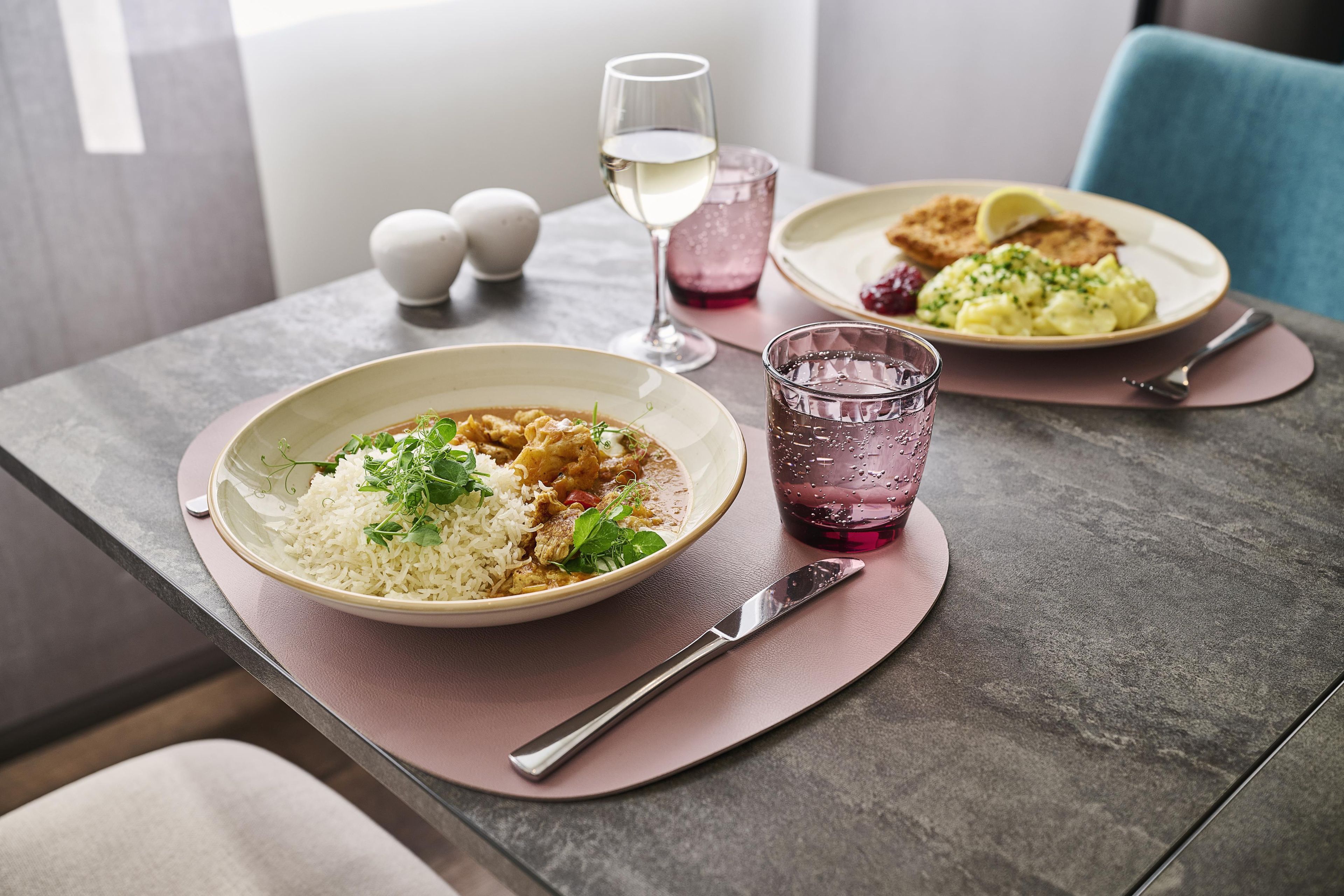 A table with a plate of food, a glass of water, and a glass of wine.