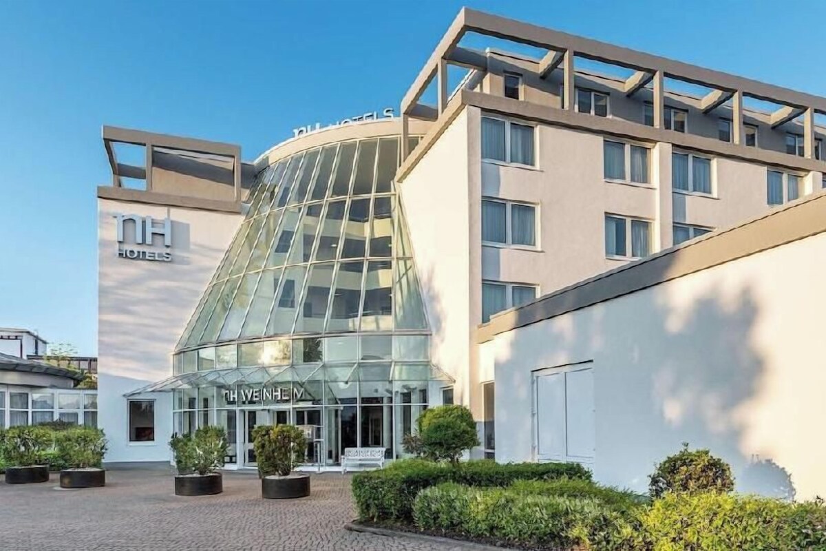 A modern hotel with a glass facade, a curved entrance, and a sign reading 'NH Hotels.'