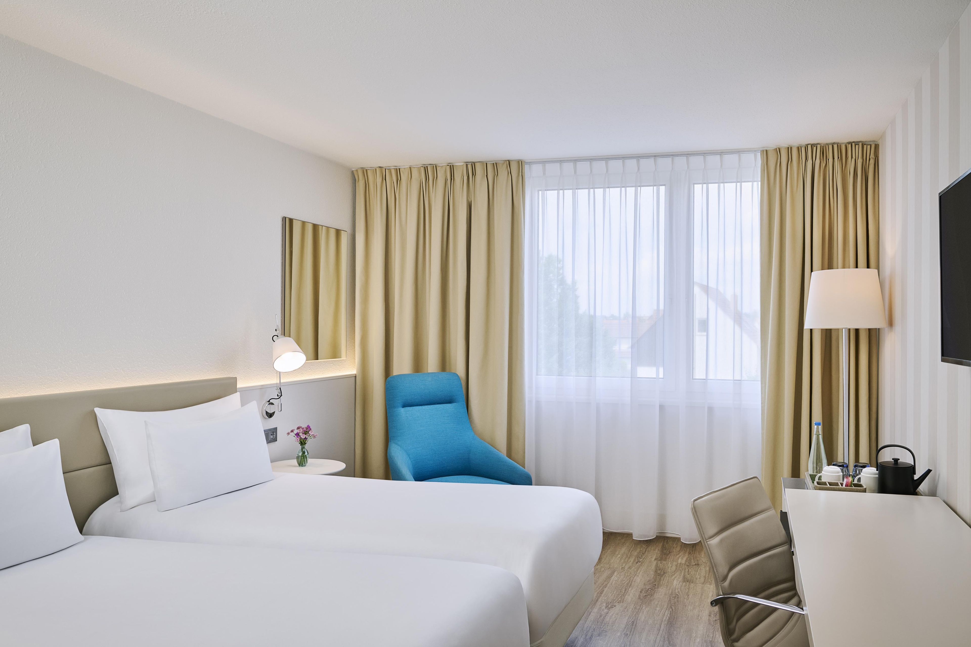 Une chambre d’hôtel avec deux lits, un bureau, une chaise, une télévision et une fenêtre avec des rideaux.
