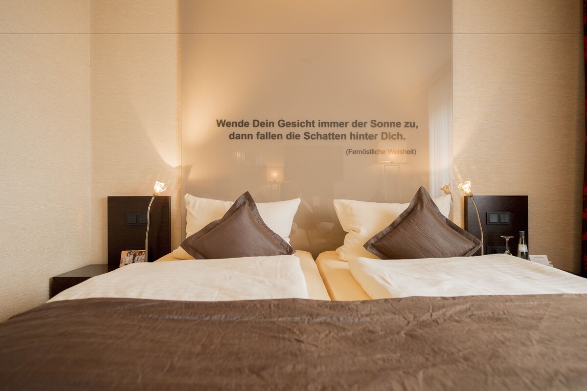 Habitación de hotel con cama, almohadas, mesitas de noche y una pared con una cita.