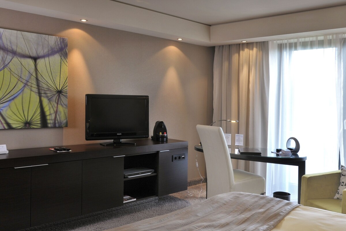 Habitación de hotel moderna con televisión de pantalla plana, un escritorio con una computadora portátil, una silla y una cama.