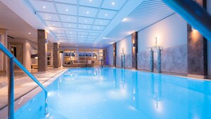 Une grande piscine intérieure avec un sol carrelé, un plafond en verre et un espace bar doté de sièges.