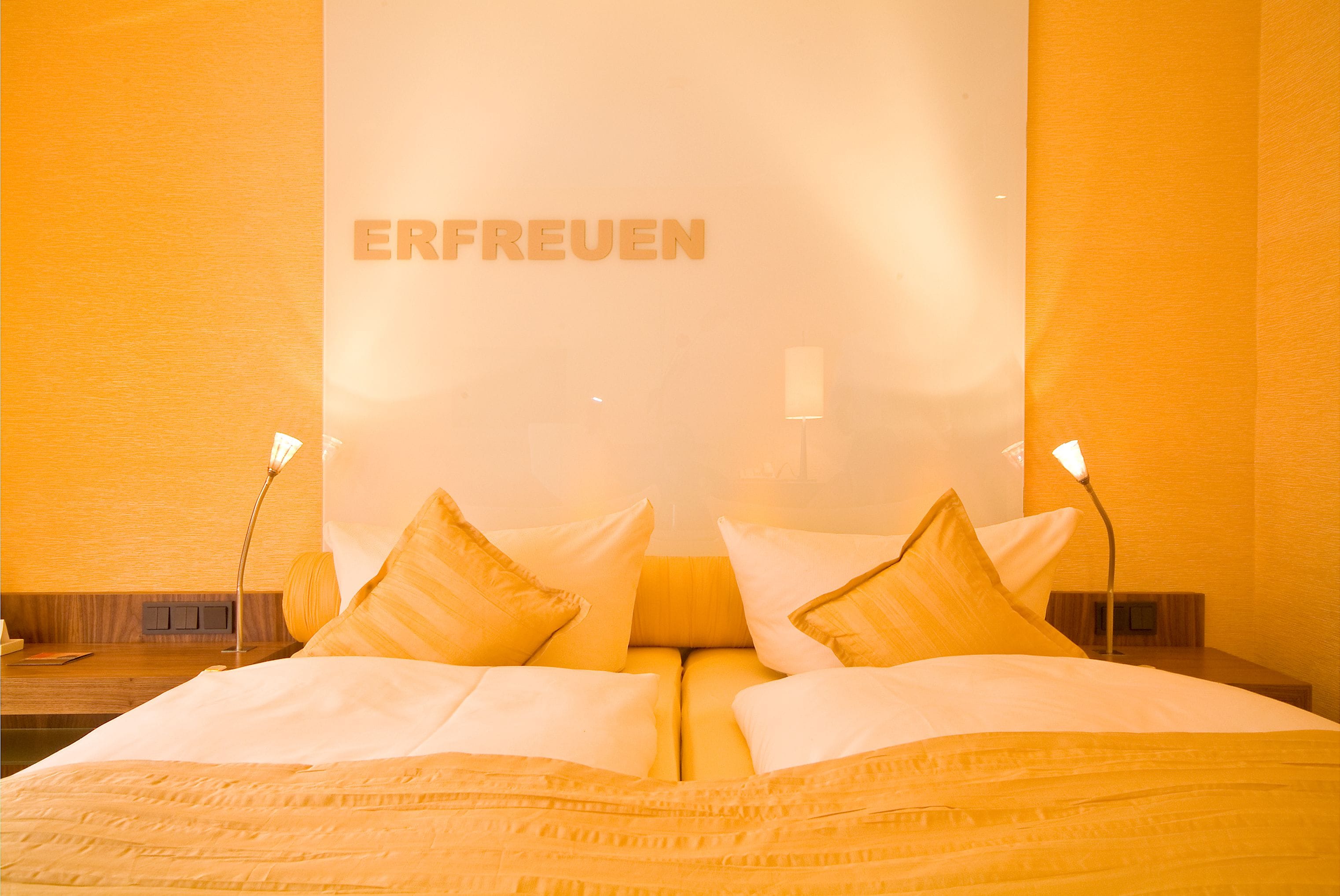 A hotel room with a bed, pillows, and a wall with the word "ERFREUEN" visible.