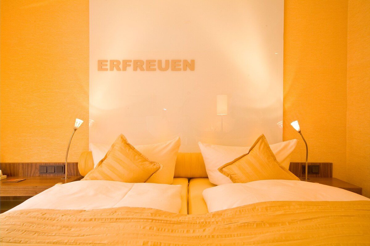 Habitación de hotel con una cama, almohadas y una pared donde se lee la palabra "ERFREUEN".