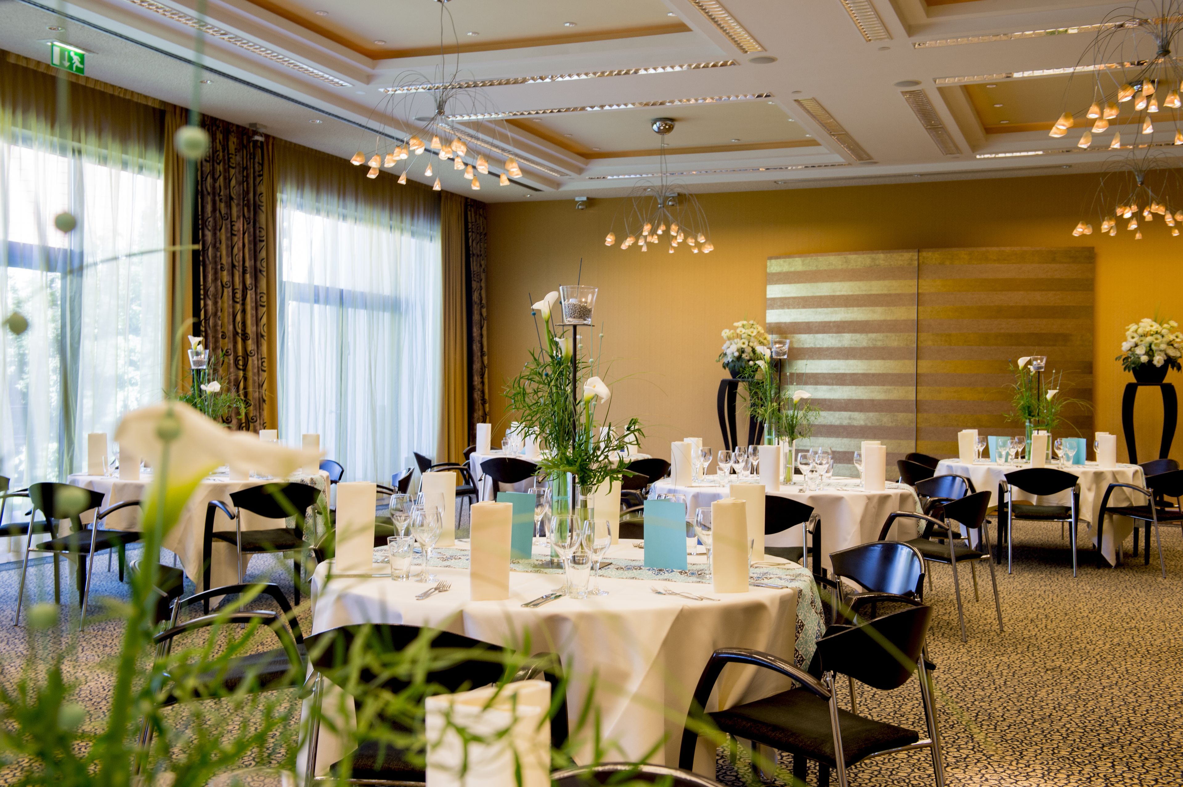 Una sala de banquets ben il·luminada amb taules preparades per a dinar, amb centrals florals i espelmaires.
